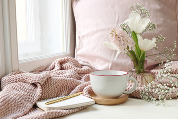 Cozy Easter, spring still life scene. Cup of coffee, notebook, golden pen, pink knitted plaid near...
