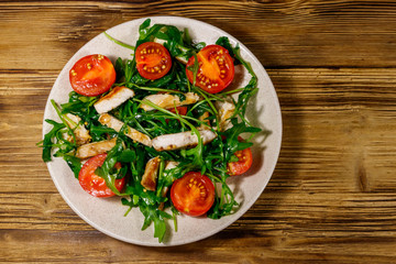 Tasty salad of fried chicken breast, fresh arugula and cherry tomatoes on wooden table. Top view