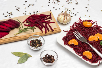 Sliced fresh beets on a cutting board. Garlic and spices. Two slices of mandarin on sliced fermented beets.