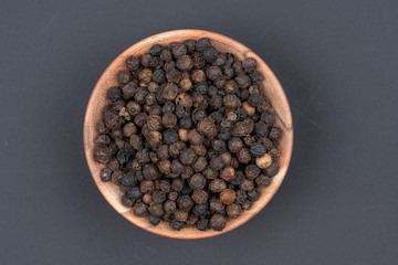 Whole black peppercorns in a small wooden bowl on a black background