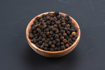 Whole black peppercorns in a small wooden bowl on a black background