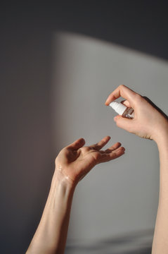 Woman hand holding and spray a sanitizer on a grey background with shadows from hand