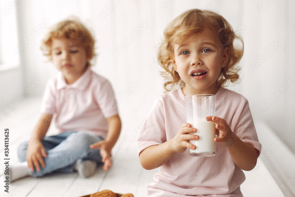 Sticker Children in a studio. Little girl with her brother. Boy in a pink t-shirt. Chold with cookies and milk.