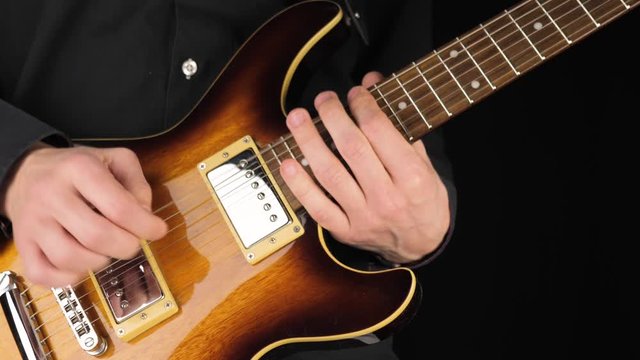 Guitarist plays a light brown six-string electric guitar with a pick against black background. Concept of stay home and make some music. Free time for sound art. Middle shot. 4K
