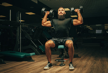 Muscular young man lifting weights in a dark gym