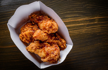 Fried breaded chicken legs in white cardboard box on wooden table background