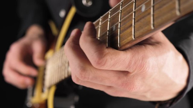 Guitarist plays a light brown six-string electric guitar with a pick against black background. Concept of stay home and make some music. Free time for sound art. Close up. 4K