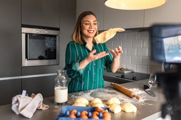 Young woman recording vlog at home in kitchen making croissants.