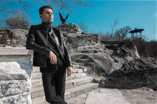 A man in a black style of clothing stands leaning on his elbow in the city of Pyatigorsk in the Stavropol Territory and looking into the distance, in the background you can see a skultpura of an eagle
