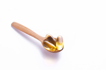 Pile of omega 3 fish liver oil capsules in wooden spoon. Big golden translucent pills on isolated background. Healthy daily fatty acids nutritional supplement. Top view, flat lay, copy space, close up