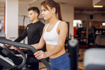 Couple in the gym. A woman performs exercises. Man in a black t-shirt