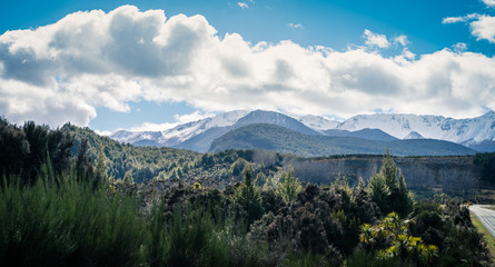 Beautiful panorama of a forest with the snow capped mountains of Milford Sound in the background taken on the SH94 road towards Milford Sound on a sunny winter day, New Zealand