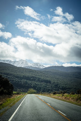 Splendid image of the SH94 road towards Milford Sound surrounded by greenery with snow capped mountains in the background taken on a sunny winter day, New Zealand