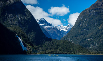 Gorgeous image of Milford Sound with a waterfall in the foreground and snow capped mountains in the background taken on a sunny spring day, New Zealand