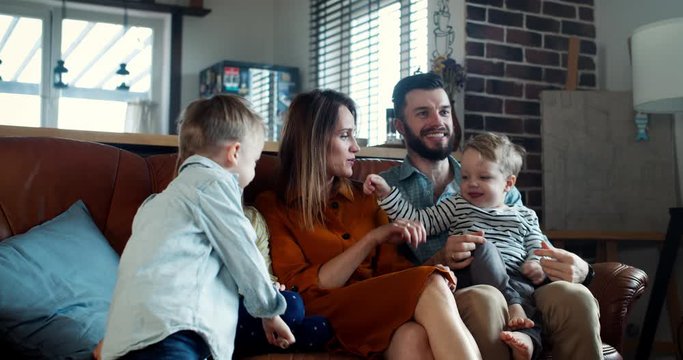 Happy family and traditional values concept, young Caucasian parents on couch together with three children slow motion.