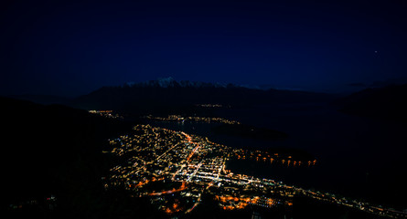 Beautiful night view of Queenstown with the snow capped mountains in the background taken during an orange sunset from the Queenstown, New Zealand Skyline