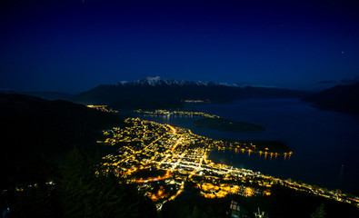 Beautiful night view of Queenstown with the snow capped mountains in the background taken during an orange sunset from the Queenstown, New Zealand Skyline