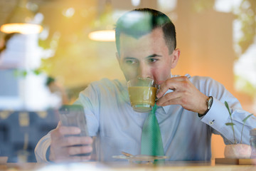 Young businessman drinking coffee while using phone at the coffee shop