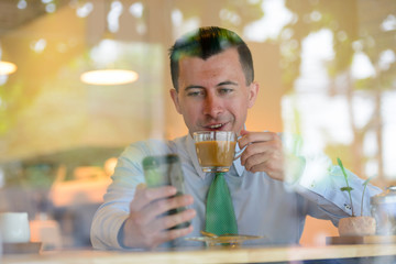 Happy young businessman drinking coffee and using phone at the coffee shop