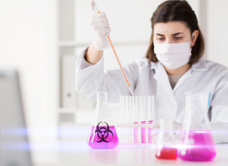 science, medicine and pandemic concept - close up of young female scientist with pipette and flask...