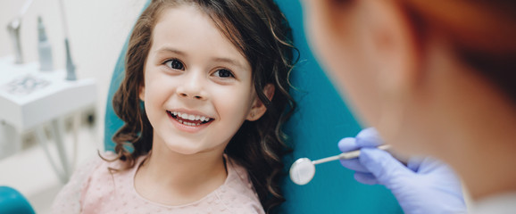 Lockiges kleines Mädchen, das nach einer Untersuchung zum Zahnarzt schaut und lächelt