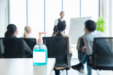 Alcohol gel bottle on table with blurred defocused group of meeting business person in background, health care personal hygiene in work place concept.