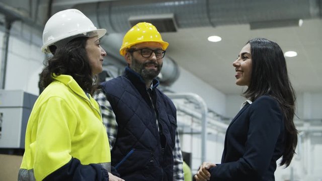 Cheerful project manager shaking hands with technicians. Side view of beautiful Asian woman in suit meeting with factory employees and greeting. Cooperation, handshake concept