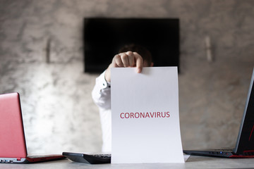 Człowiek w biurze z kartką w dłoni z napisem coronavirus - obrazy, fototapety, plakaty