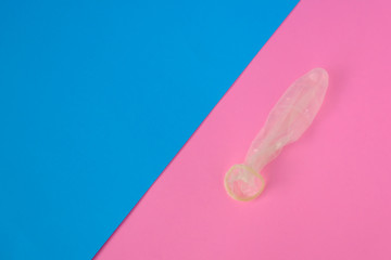 Used condom on pink and blue paper background with copy space for text. Reproductive health, contraception and safe sex concept