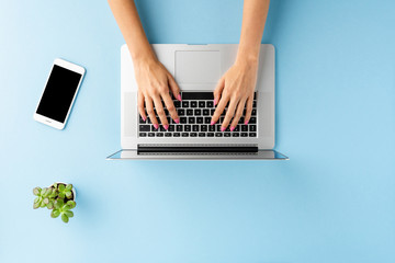 Female hands working on modern laptop on blue background with accessories. Office desktop. Flat lay