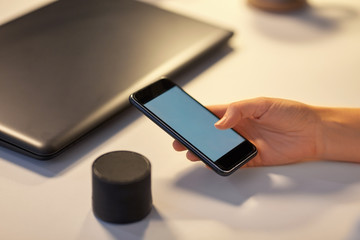business, technology and internet of things concept - hand with smartphone and smart speaker at...
