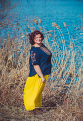 Plus size woman in embroidered shirt and yellow skirt at nature, fashionable clothes