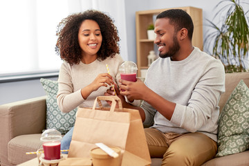eating and people concept - happy african american couple with takeaway food and drinks at home