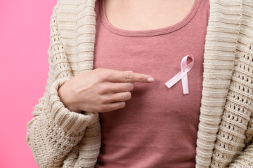 Midsection of a woman pointing to a pink breast cancer awareness ribbon on her Tshirt isolated over...