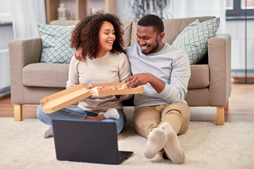 leisure, people and food concept - happy african american couple with laptop computer eating takeaway pizza at home