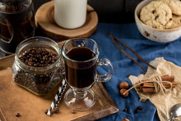 Obraz na płótnie Canvas Cup of coffee with coffee beans, spoon, cinnamon sticks, bottle of milk and cookies on blue background