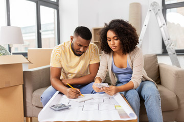 mortgage, moving and real estate concept - african american couple with blueprint and calculator...