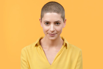 Studio portrait of a beautiful young caucasian woman with shaved head against bright yellow...
