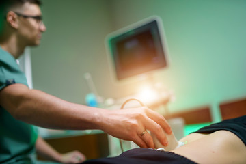 A young male doctor makes a patient an ultrasound of the abdominal cavity. Ultrasound scanner in...