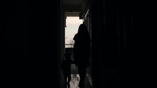 young mother and little girl walk hand in the street in the backlight