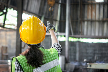 Back side of industrial engineer worker female wearing helmet standing and pointing something at manufacturing plant factory, woman working in industry