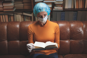 Woman with protective antiviral mask sitting at home in isolation / quarantine and reading book.