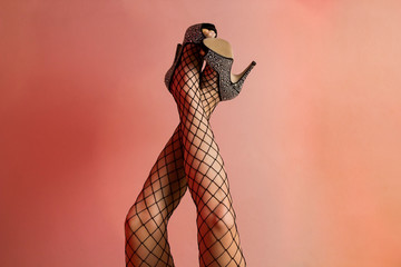 Beautiful woman legs with black stockings high heel shoes against a white wall with red lights reflecting on the wall.