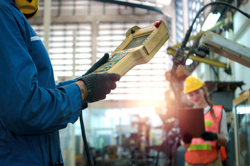 Industrial engineer worker working with control panel of robot arm for arduino mechanism at manufacturing plant factory, young people working in industry