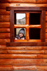 Little girl looks out the window of a wooden house in the playground in an eco-park