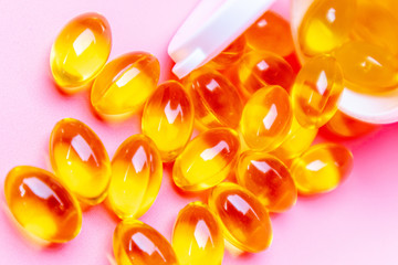 Dietary supplement gel capsules. pills spilling out of prescription bottle on pink background.