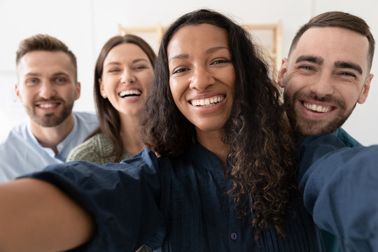 Smiling multiracial colleagues take self-portrait picture have fun entertaining together in office, happy diverse coworkers laugh make selfie on gadget at workplace together, relax during work break