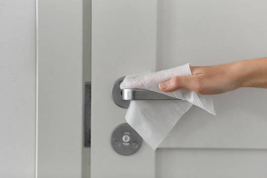 hygiene, health care and safety concept - close up of hand cleaning and disinfecting door handle surface with antiseptic wet wipe