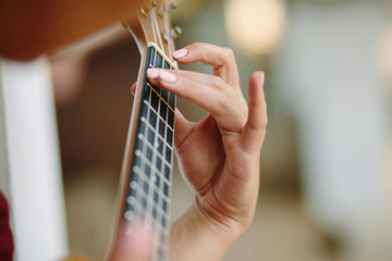  The girl plays on the ukulele, fingers clamping the chord of a guitar. 