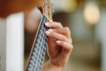 The girl plays on the ukulele, fingers clamping the chord of a guitar. 